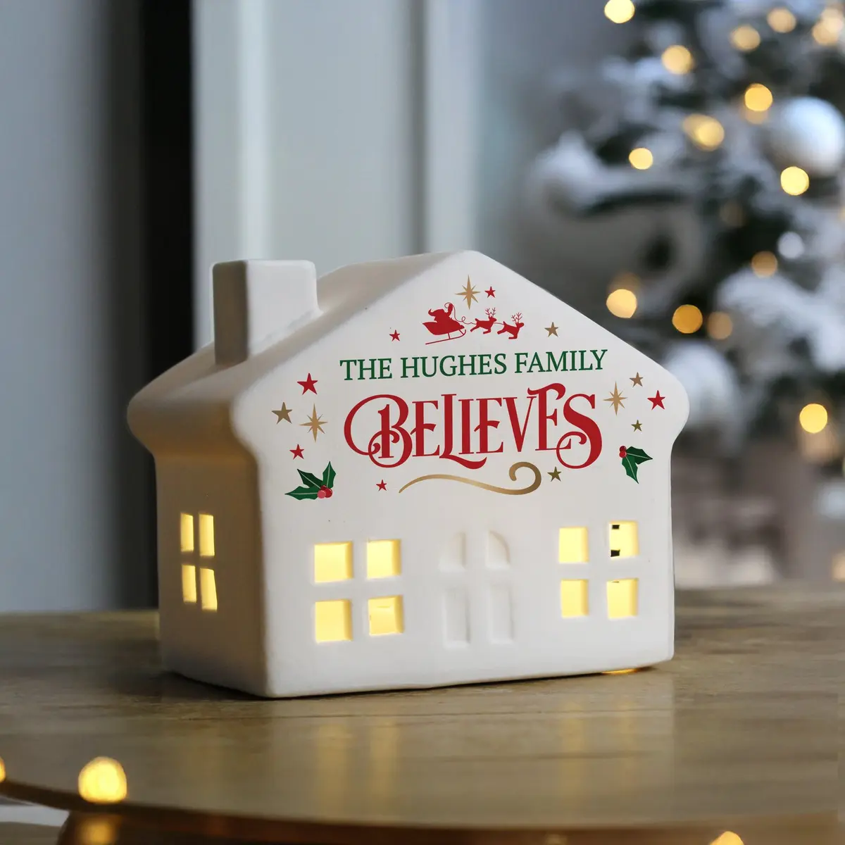 Ceramic light-up Christmas house with cut-out windows and a name above believes